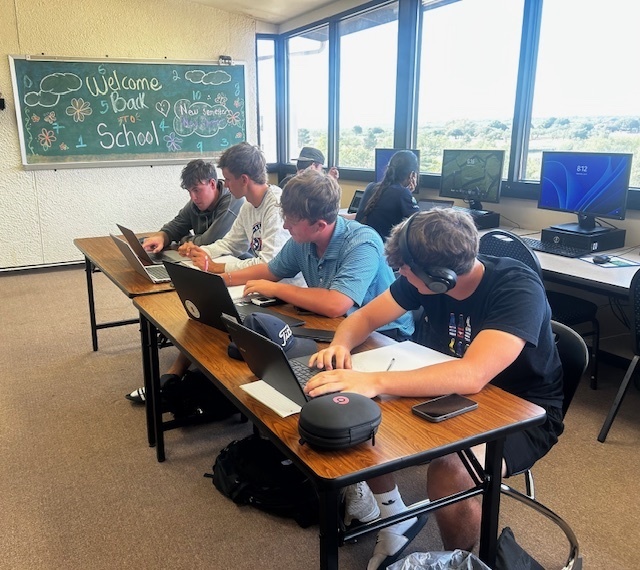 Students study at a row of desks while a tutor helps a students on the end.