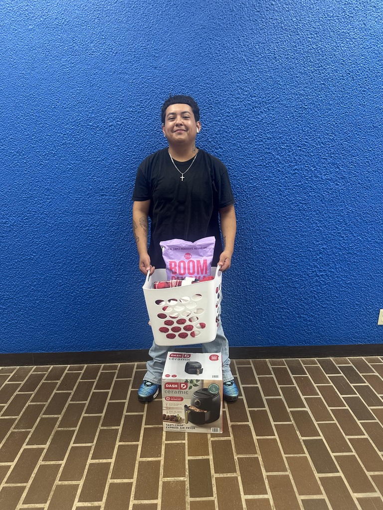 Dominick Lopez stands smiling  with his prizes against a blue wall.