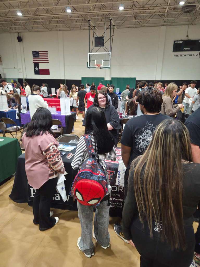 A student wearing a Spider-Man backpack talks to a representative at a black-covered booth during the college fair.