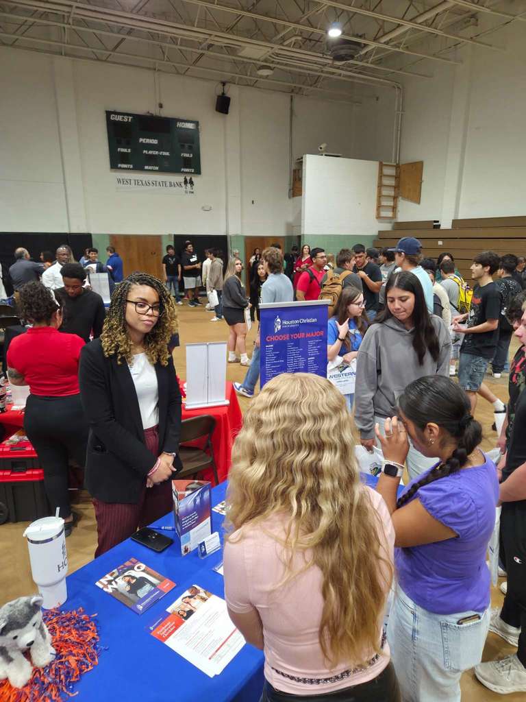 Two students talk with a Houston Christian University representative at a blue-covered booth during the college fair.