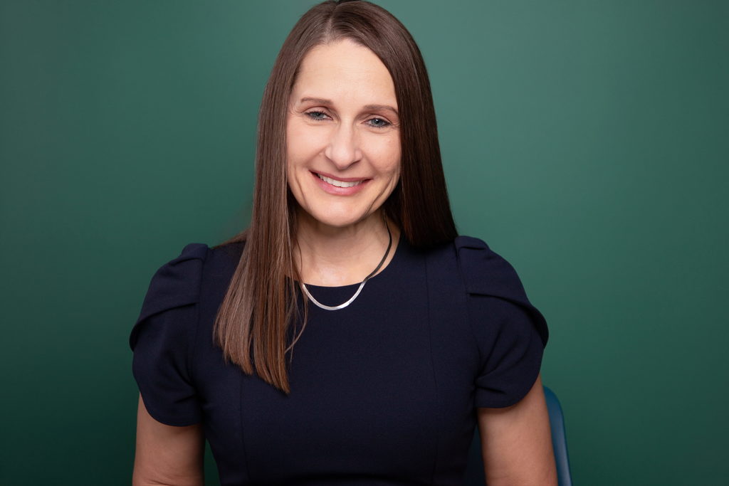 A photo of Dr. Laurie Sharp standing against a green background.