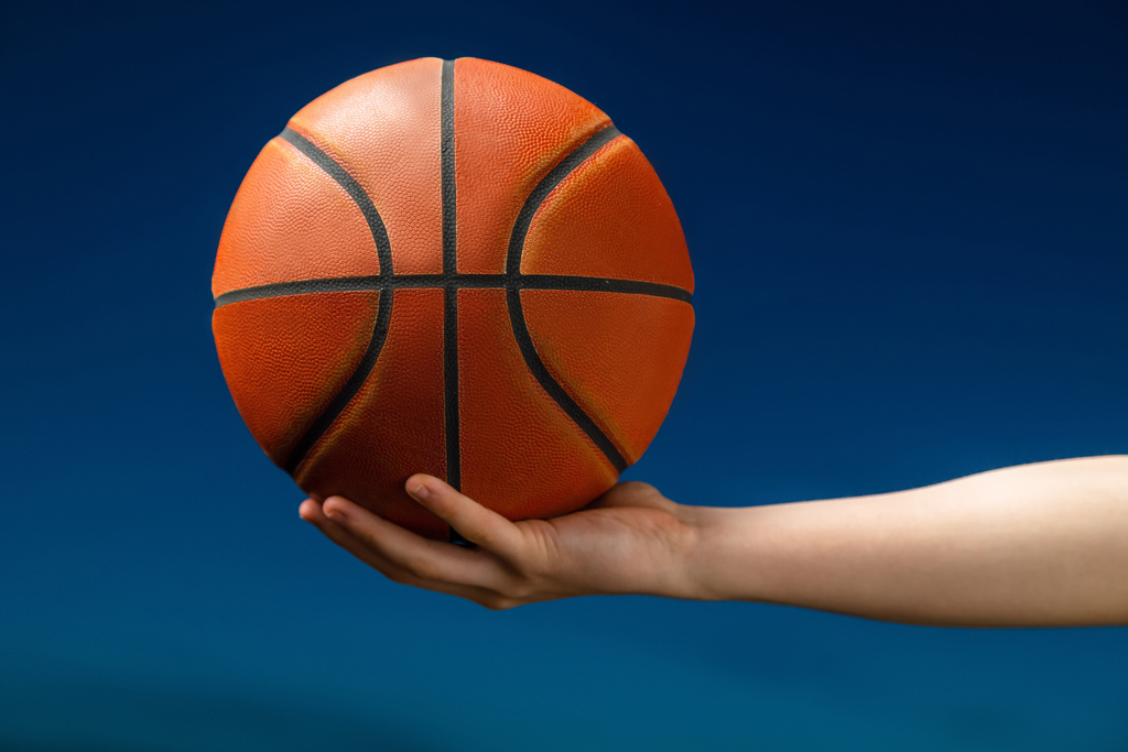 An open hand hold an orange basketball against a blue background.