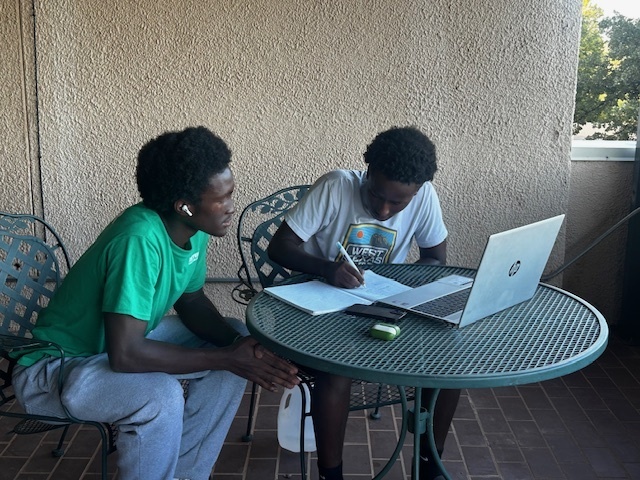 Two students studying outdoors at a metal table, using a laptop and notebook at Western Texas College.