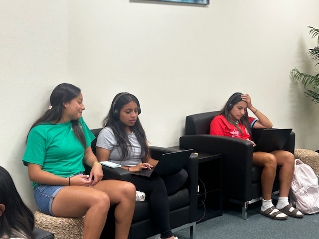 Three students sitting in a lounge area using laptops for studying.