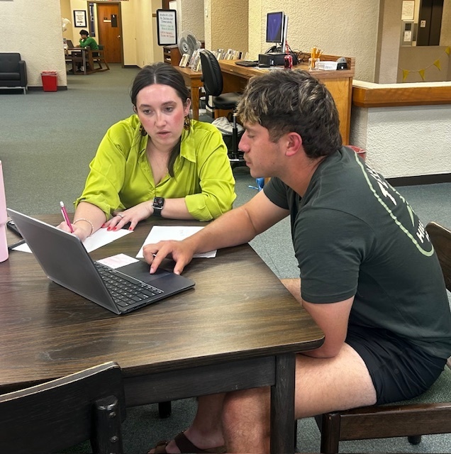 Tutor and student collaborating at a table, reviewing notes beside an open laptop.