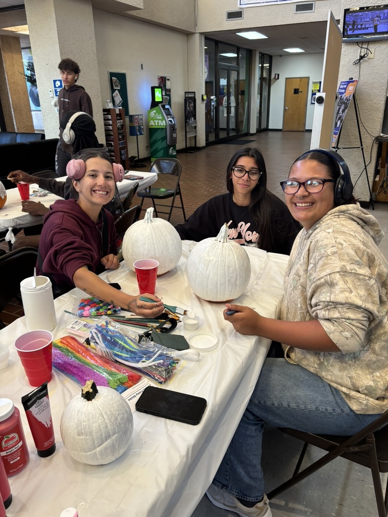 Three students smiling while painting pumpkins together at the decorating contest.