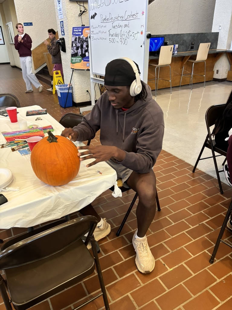 Student wearing headphones decorates a pumpkin at a table during the contest.