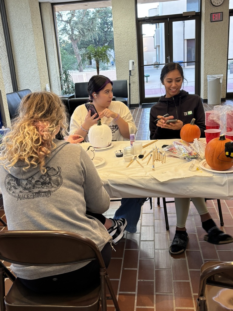 Three students sitting together at a table painting pumpkins and chatting for the decorating contest.