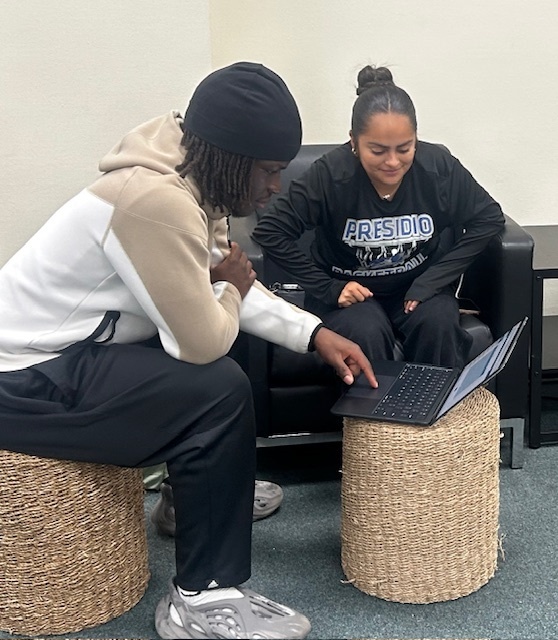 A tutor helps a student while they look at a laptop in the Library.