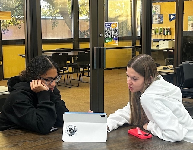 A tutor helps a student sitting at a table in the Library.