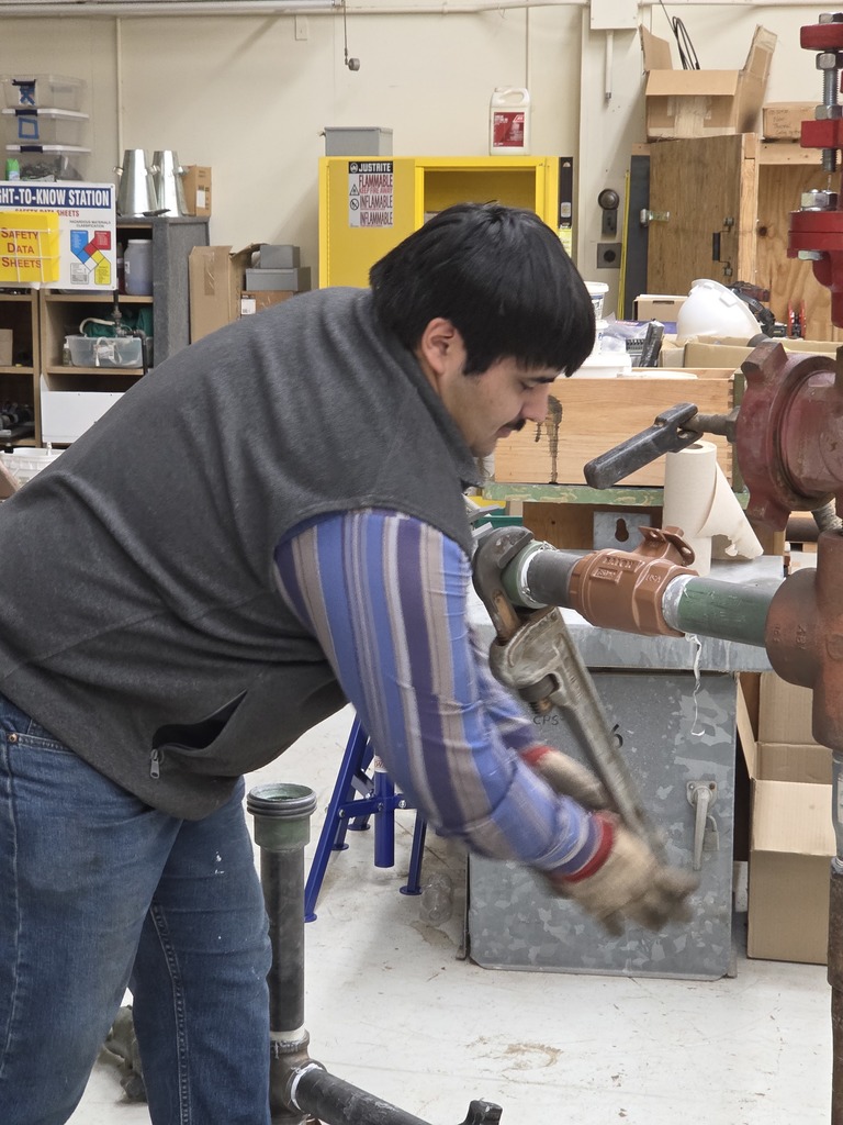 A student tightens a pipe fitting with a large wrench during oilfield technology training.