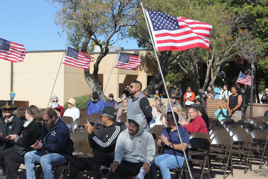Veterans stand as attendees applaud during the ceremony surrounded by American flags.