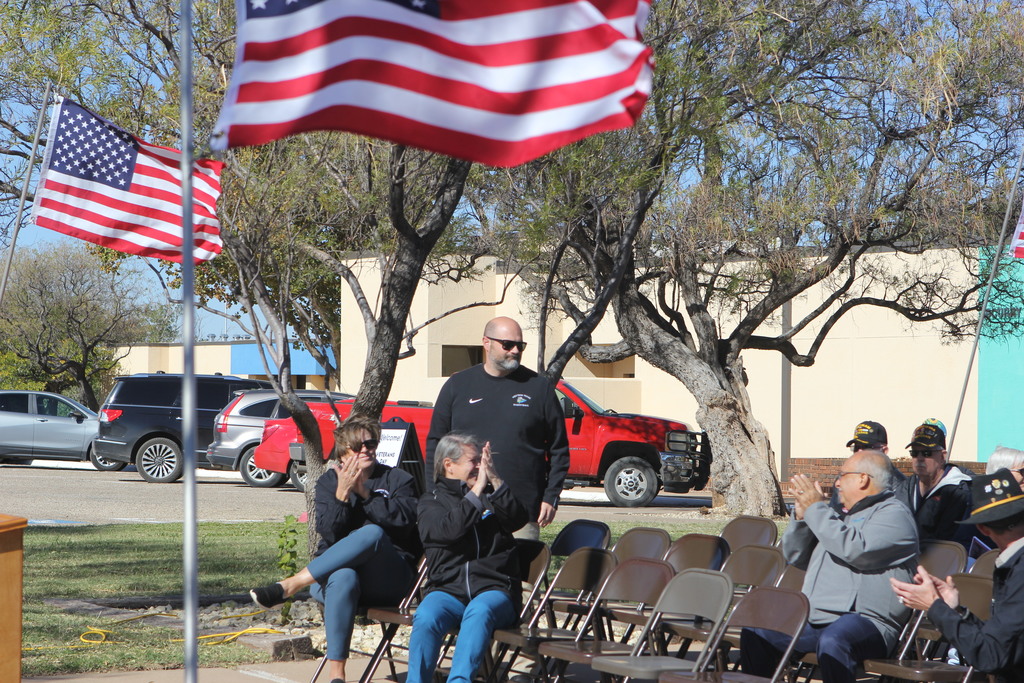 Veteran stands as attendees applaud during the ceremony surrounded by American flags.