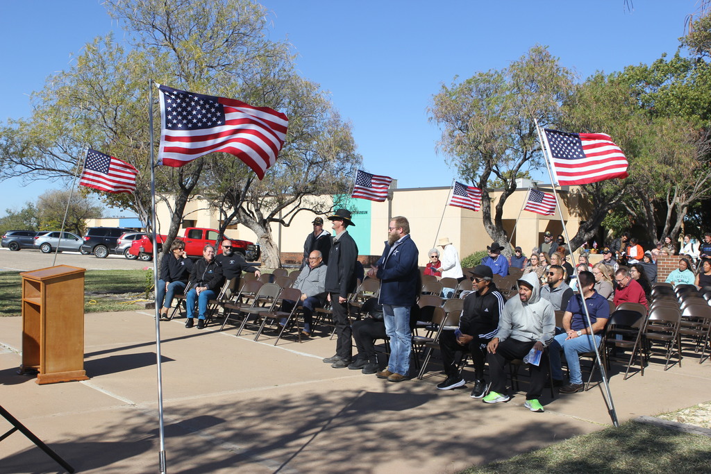 Veterans stand as attendees applaud during the ceremony surrounded by American flags.