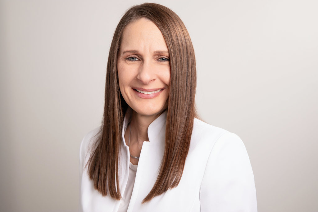 Dr. Laurie Sharp smiles while standing against a light beige background.