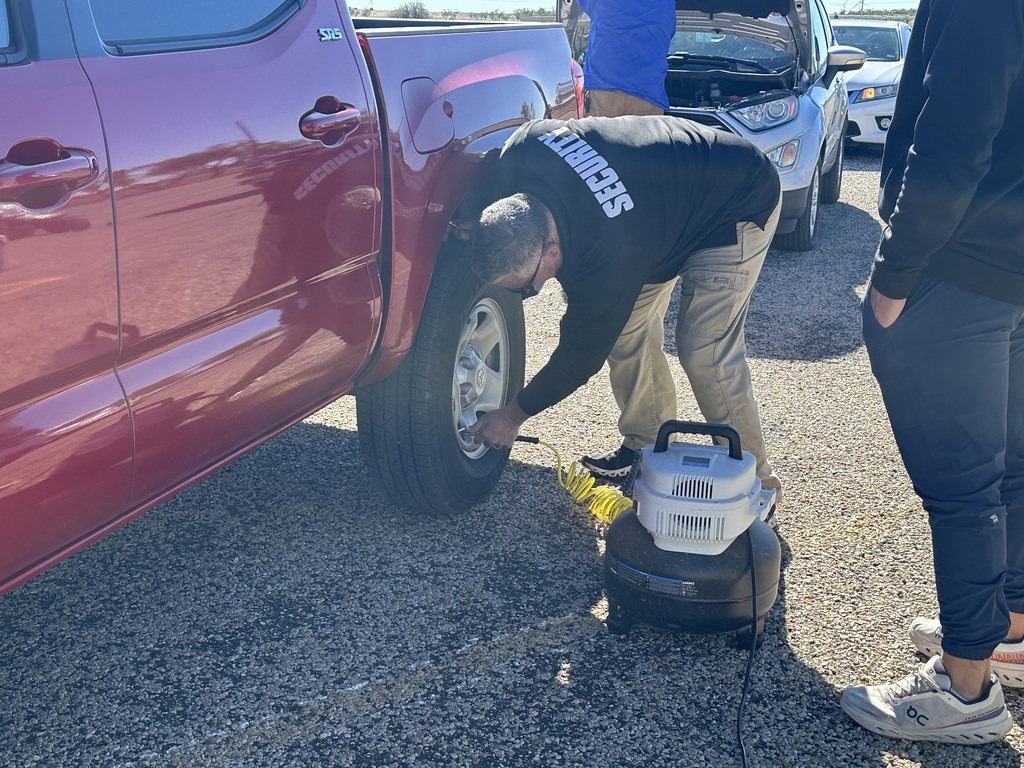 The Director of Security checks air pressure in a tire while a student watches.