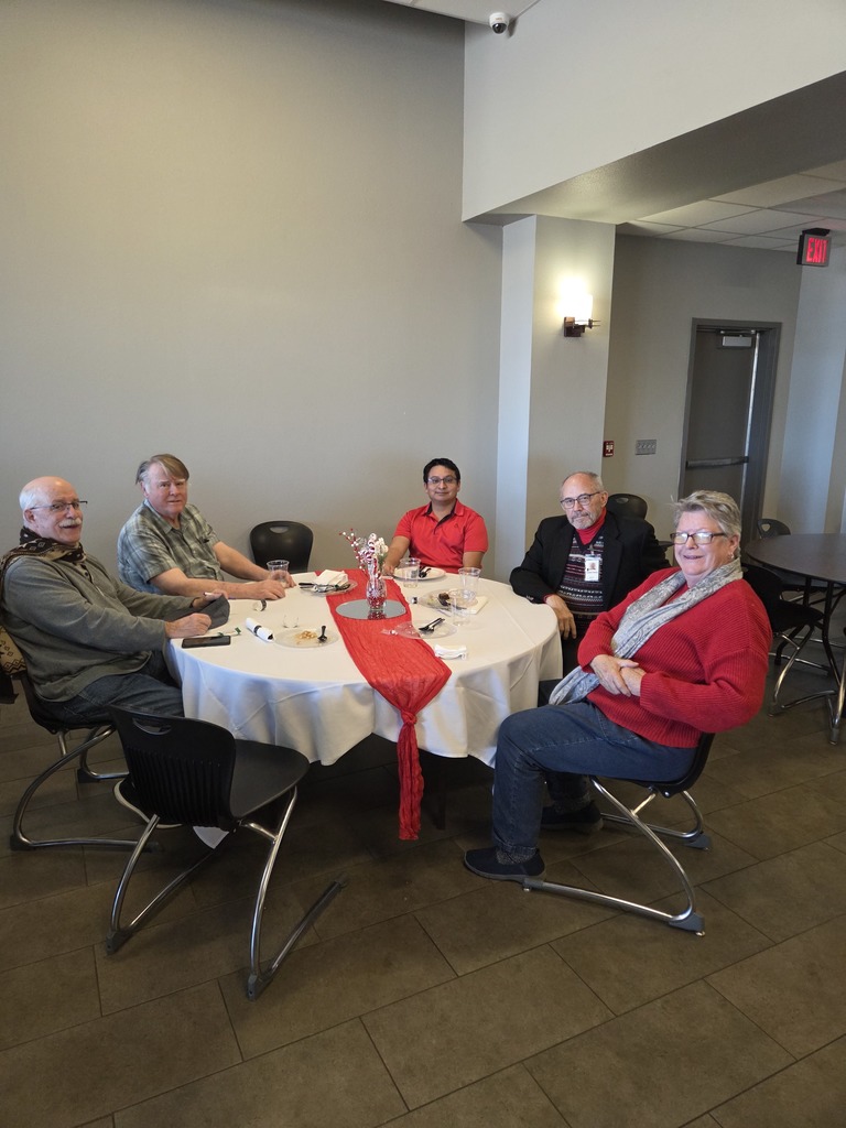 Five faculty members seated at a round table with red table runner during the potluck luncheon.