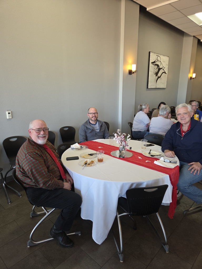 Three faculty Five faculty members seated at a round table with red table runner during the potluck.