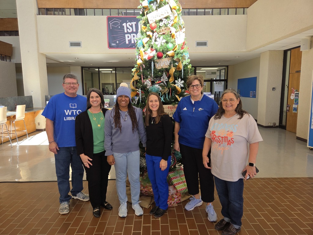 Group of Western Texas College employees standing in front of a decorated Christmas tree in a Student Center lobby.