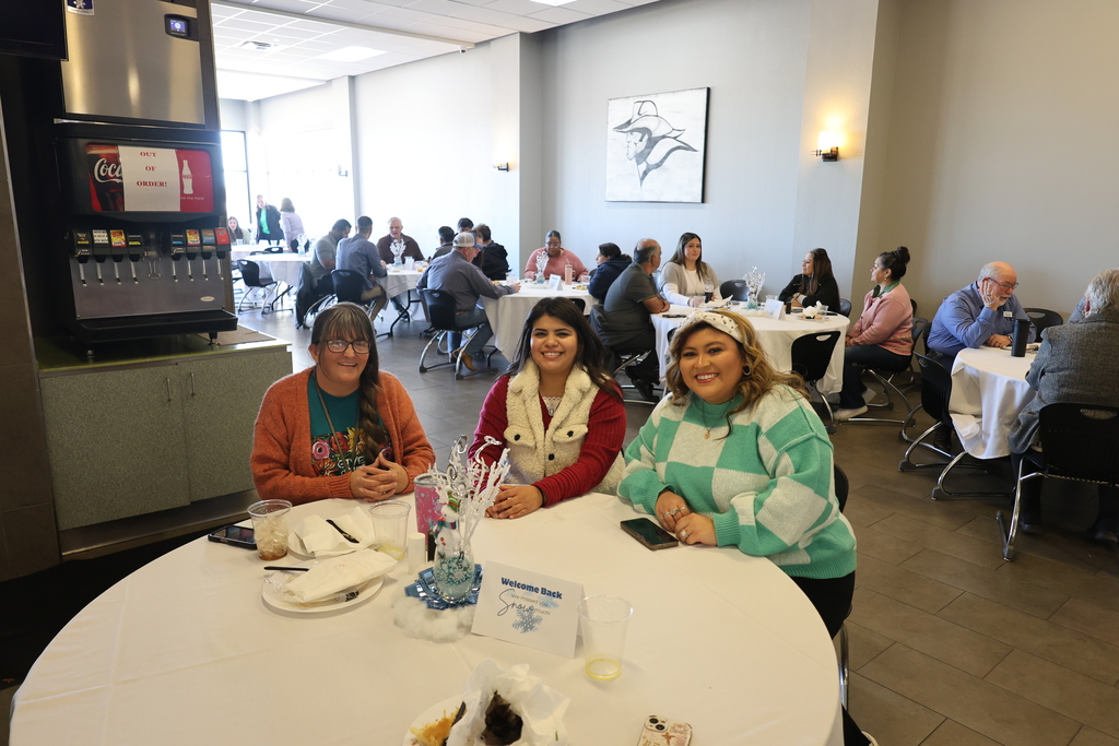 Amy, Cassie and Naudia smile while sitting at a table covered in a white tablecloth in the cafeteria.