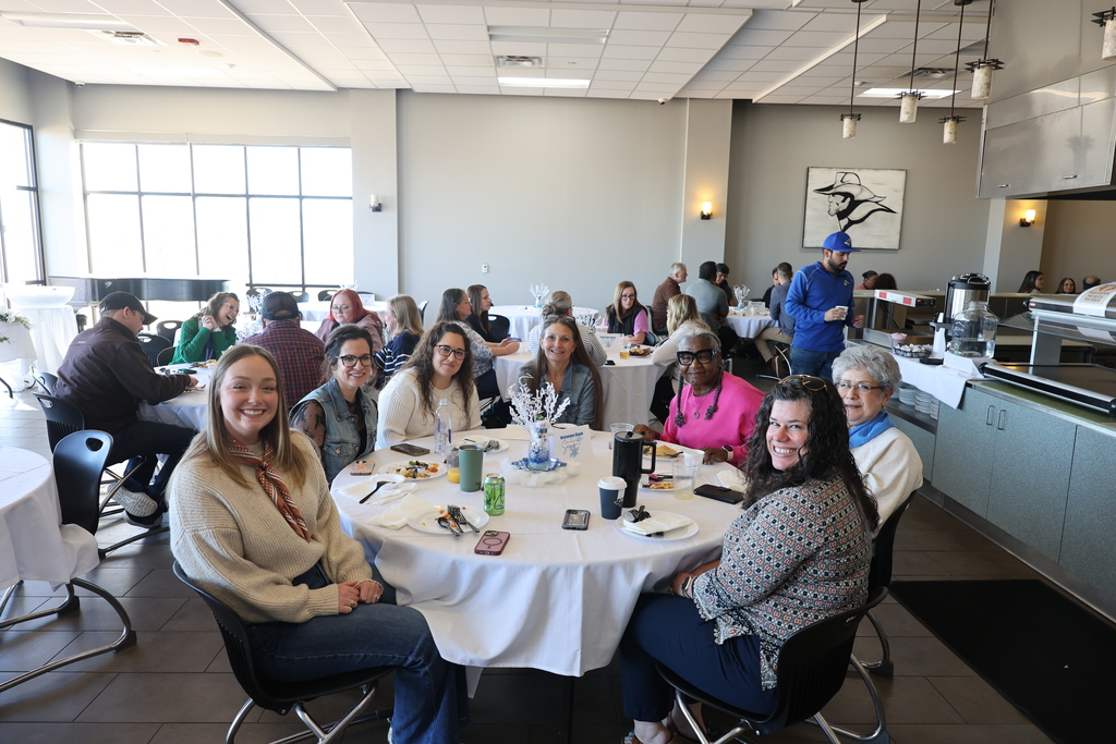 Talent search and Upward Bound staff smile while sitting at a table covered in a white tablecloth in the cafeteria.