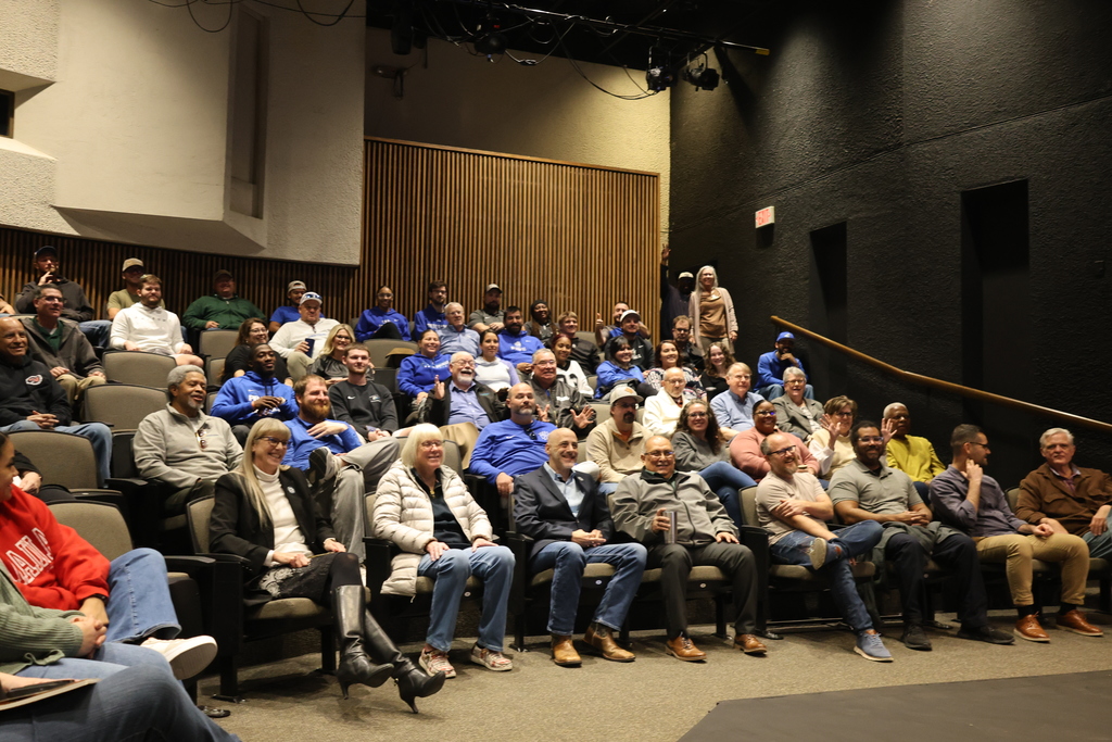 Employees sitting in the audience of the Fine Arts Theater smile at Dr. Sharp.