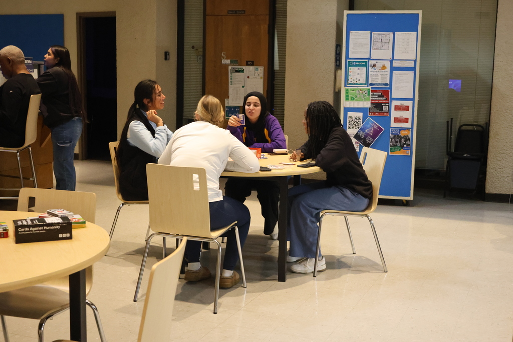 Students lean over a table, focused on a card game at WTC Student Center Game Night.