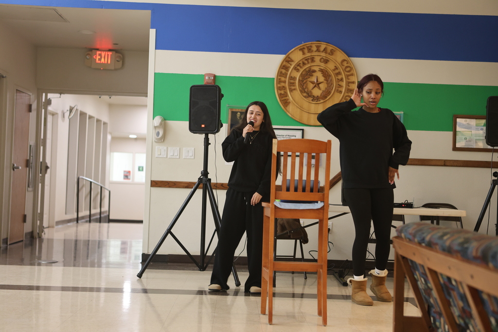 Student and coach  perform karaoke with microphones during open mic night in the WTC Student Commons.