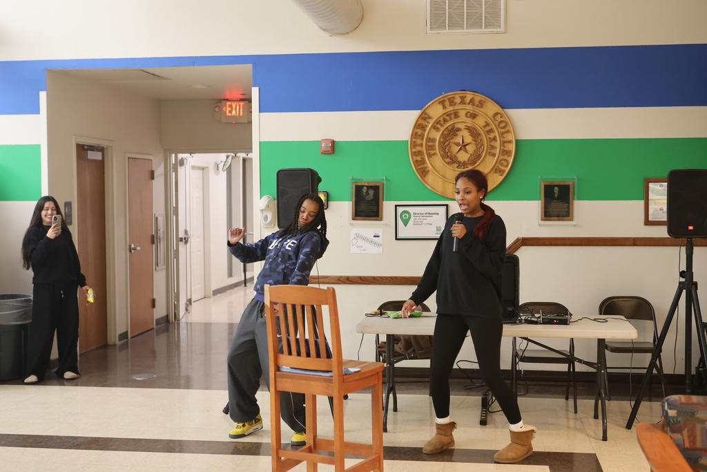 A coach sings karaoke while another dances nearby in the WTC Student Commons.