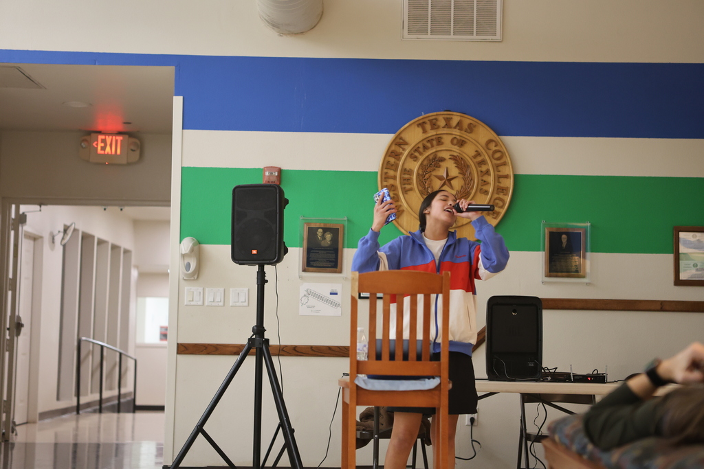 A student sings karaoke into a microphone near the Western Texas College seal.