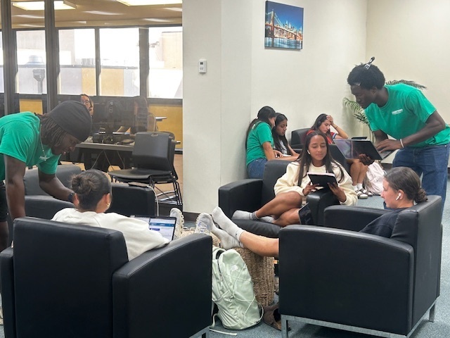 Tutors in green t-shirts help students sitting in chairs in the Library.