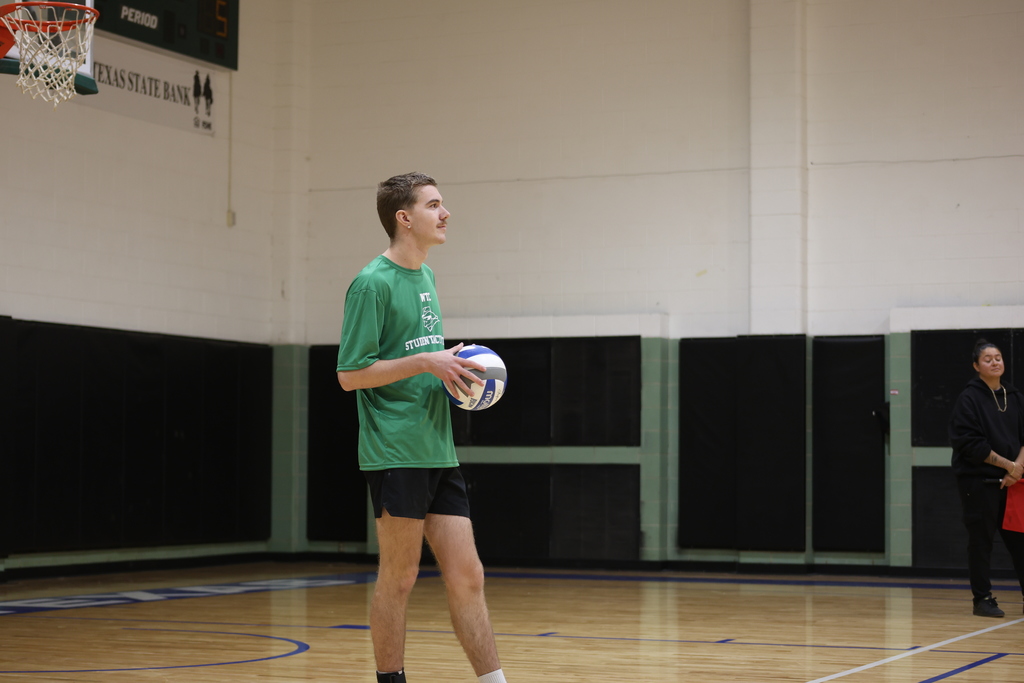 A player in a green shirt stands on the court holding a volleyball before serving.