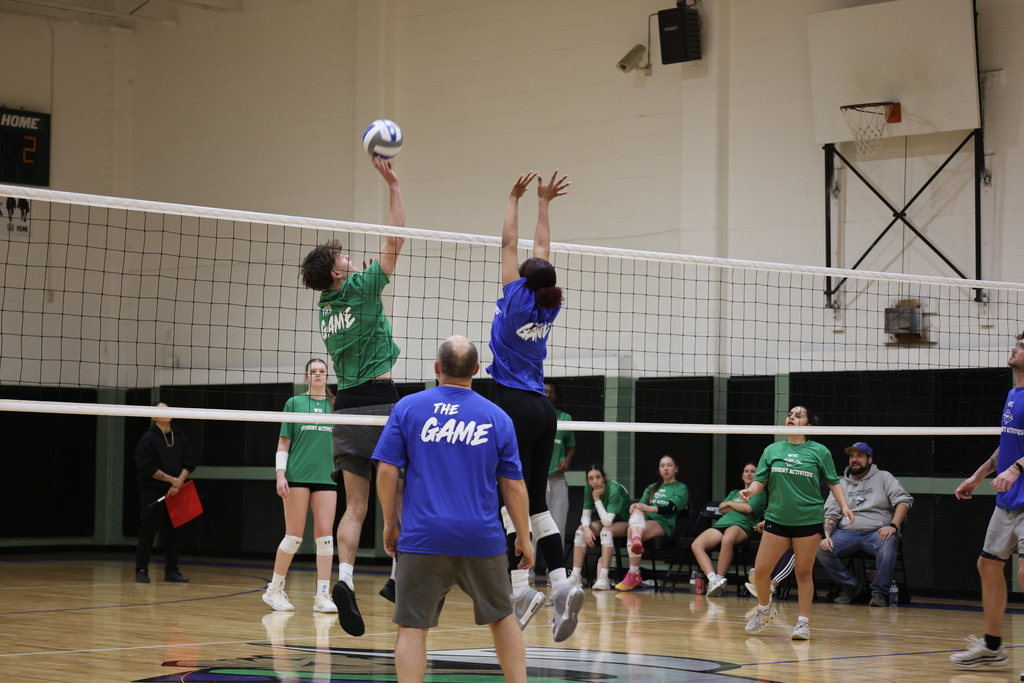 Two players jump at the net attempting a block during an indoor volleyball match.