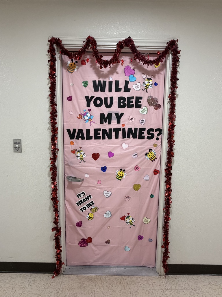 Pink Valentine’s door reading “Will you bee my Valentines?” decorated with bees, hearts, and red garland.