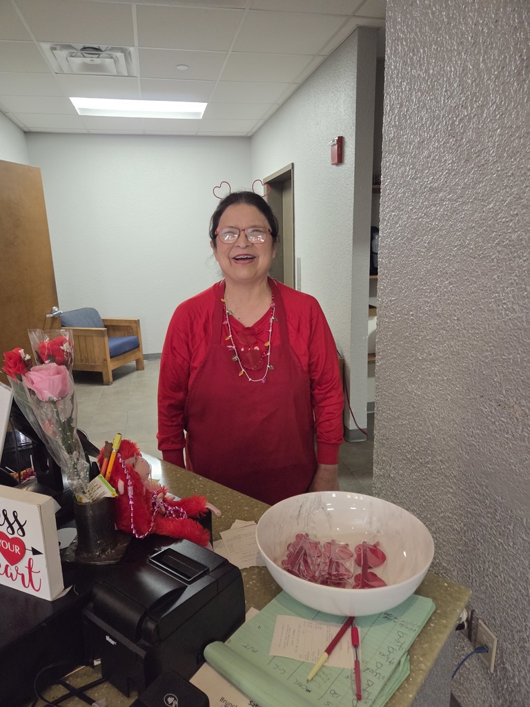 Staff member in red shirt stands behind counter with heart decorations and Valentine candy bowl.