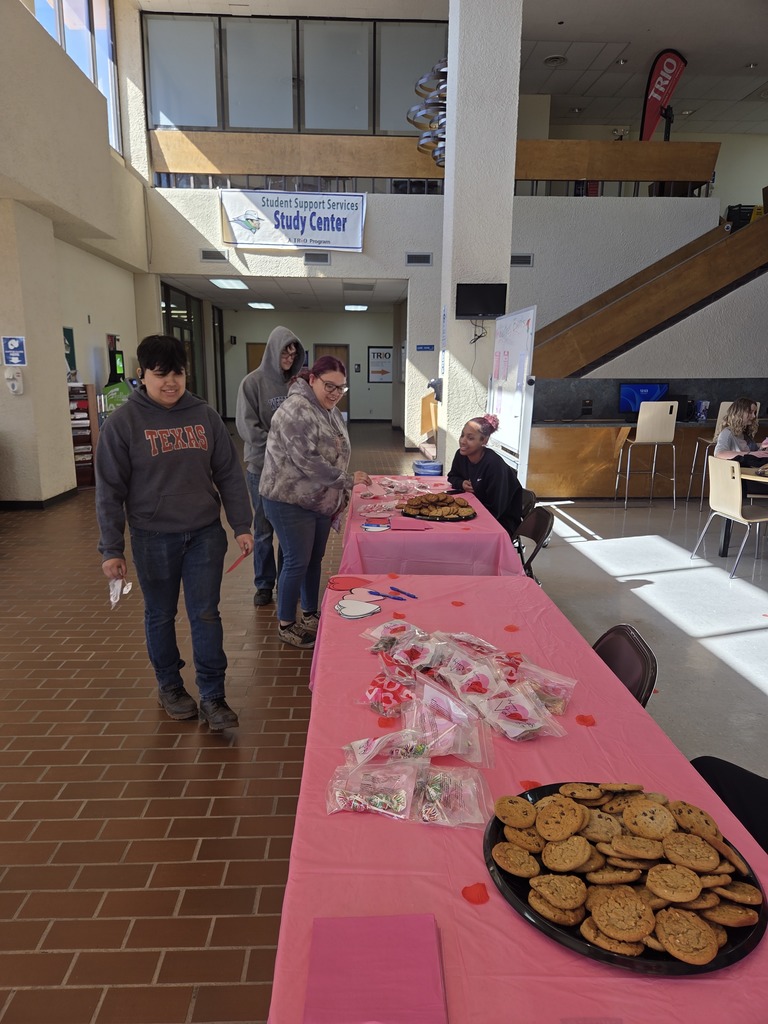Students walk through lobby toward Valentine treat table with cookies and heart-themed gift bags.