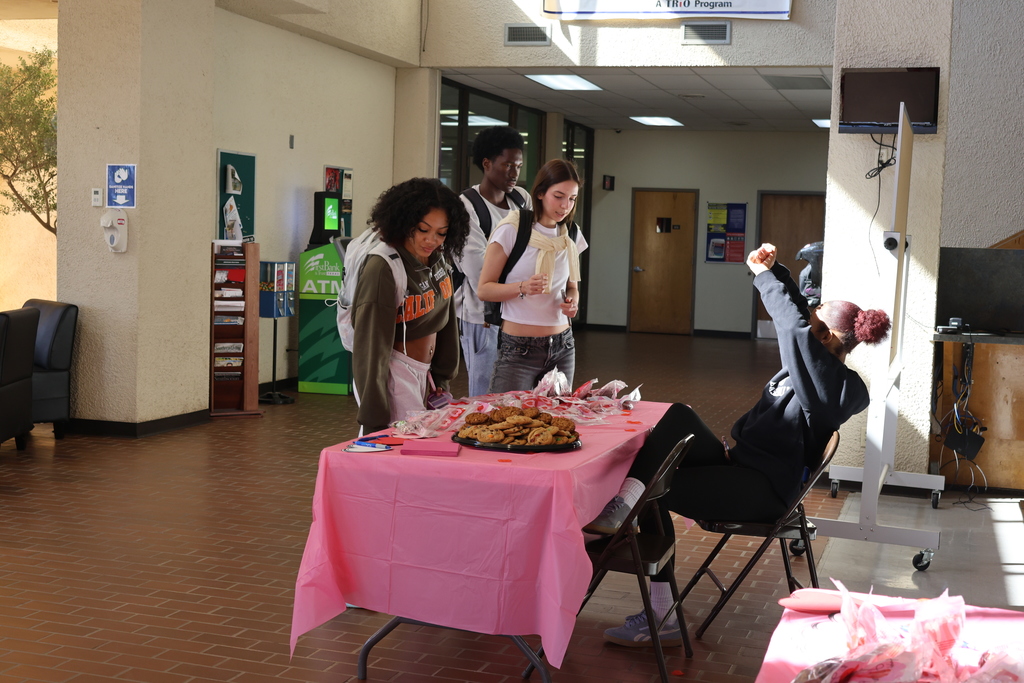 Students smile while choosing Valentine treat bags and cookies in campus lobby.