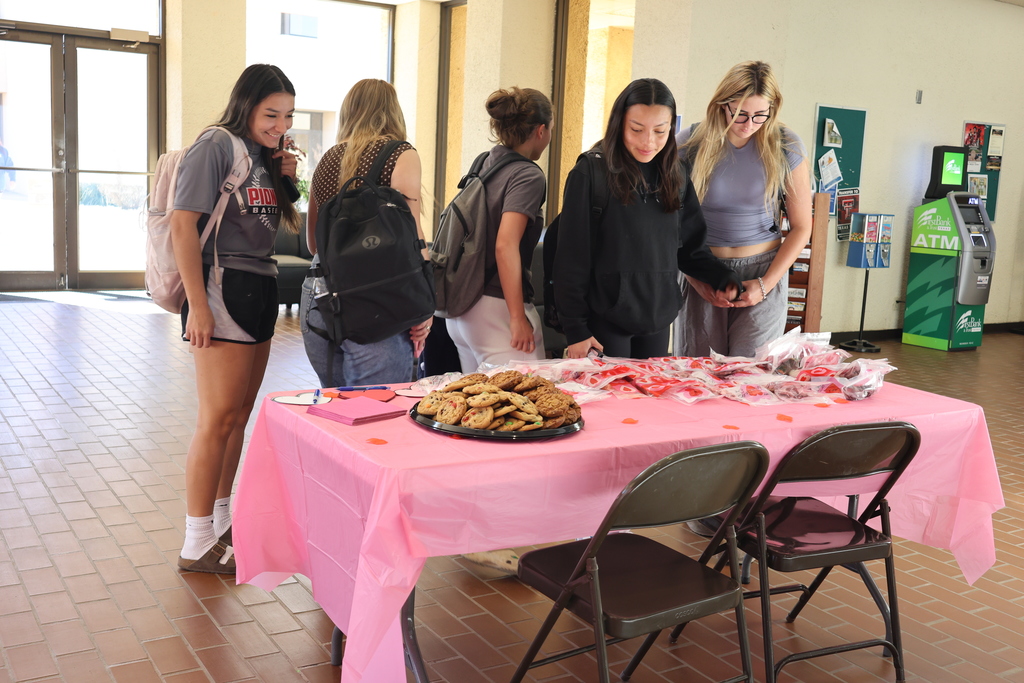 Students smile while choosing Valentine treat bags and cookies in campus lobby.