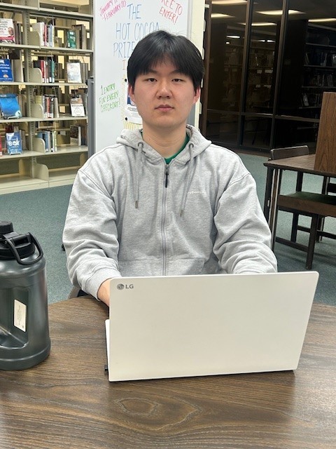 A man sits at a table with an open laptop in front of him.
