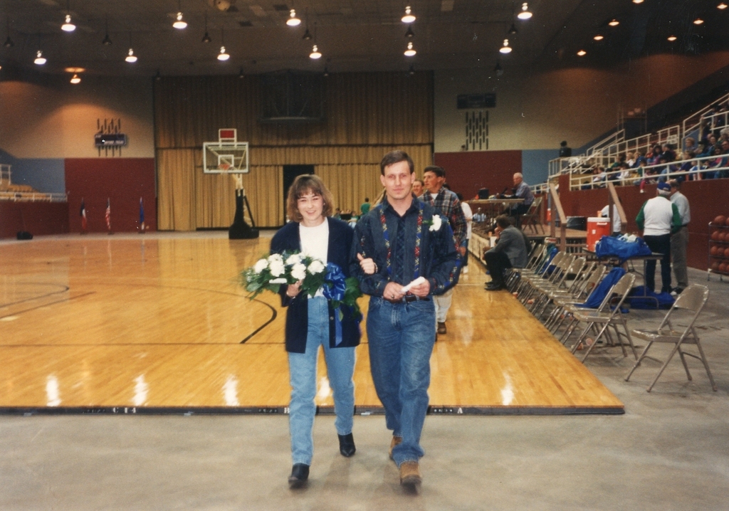 A man escorts a woman on a basketball court.