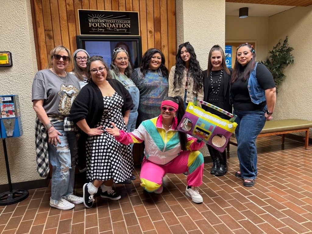 A group of people posing in a foyer dressed to represent different decades.