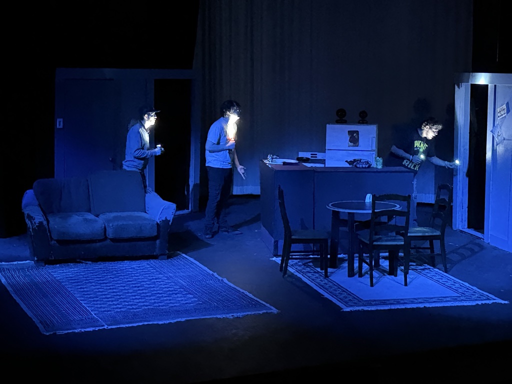Stage scene with three actors exploring dark set using flashlights during Western Texas College production of The Boys Next Door.