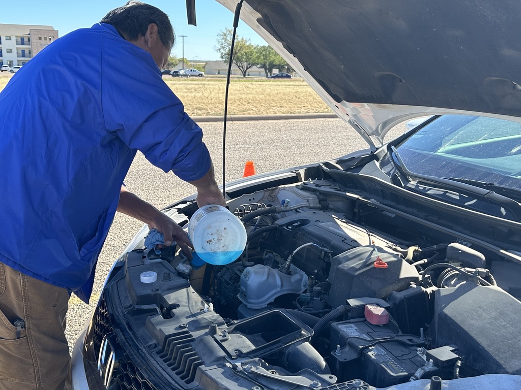 A man pours windshield wiper fluid into the reservoir in the engine of a vehicle.