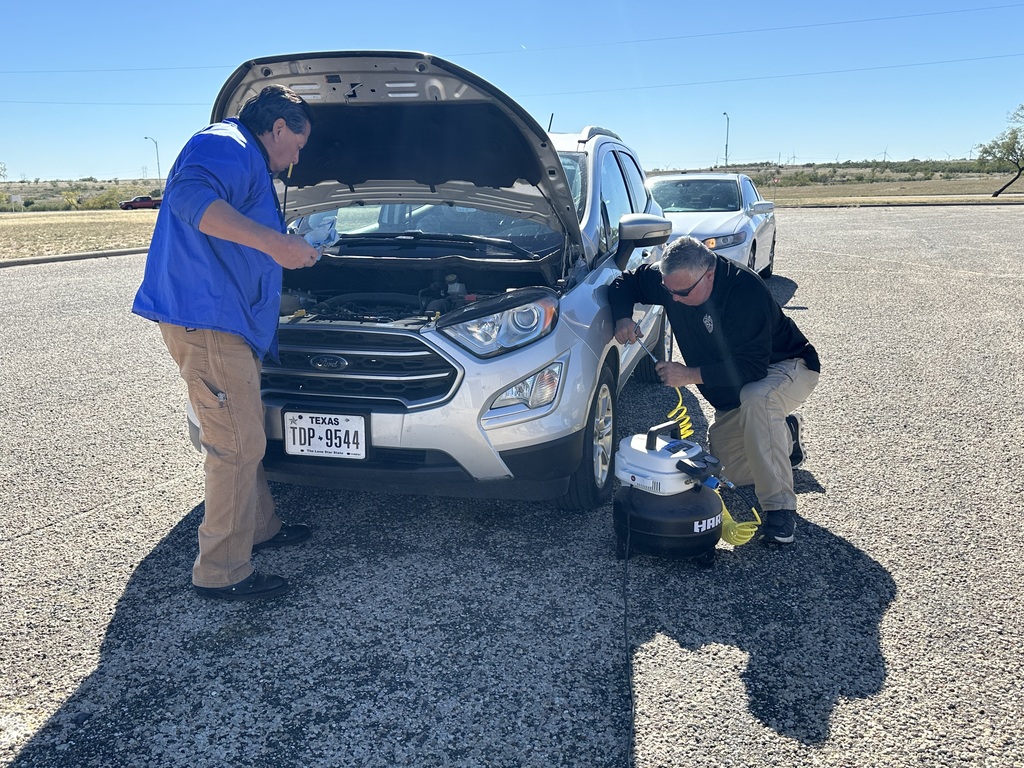 Two men check air pressure and oil on a car.