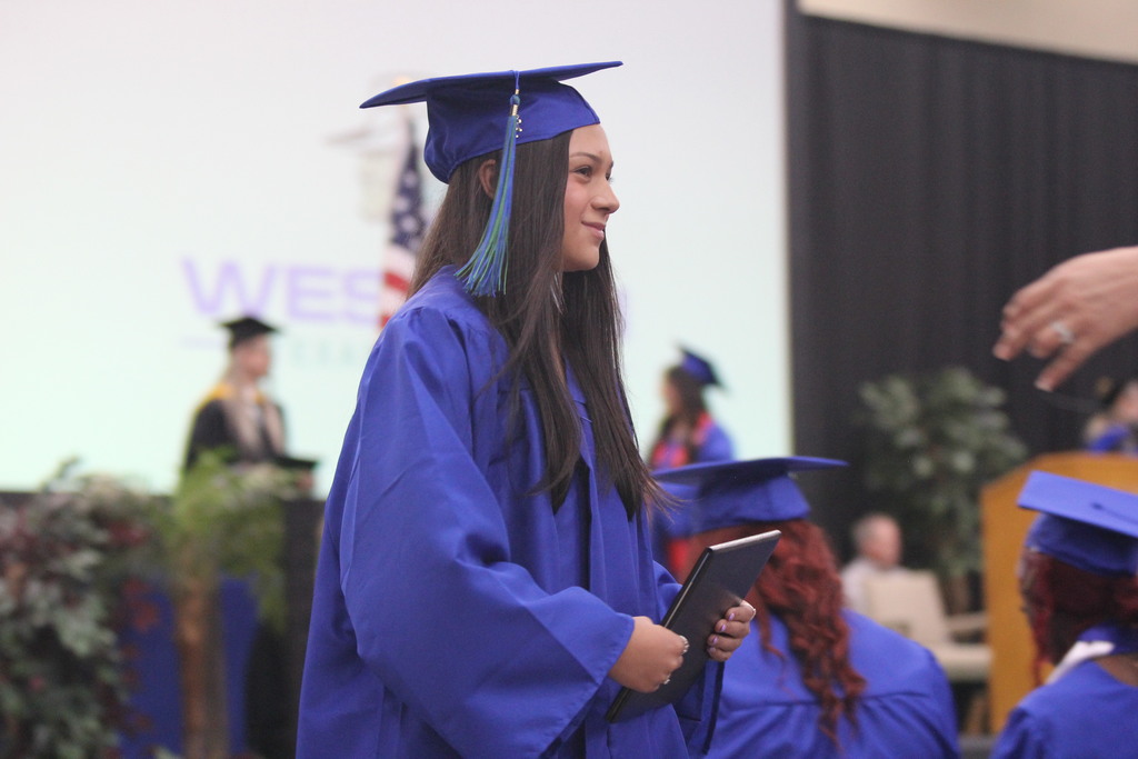 A graduate smiles holding  a diploma walking back to their seat.