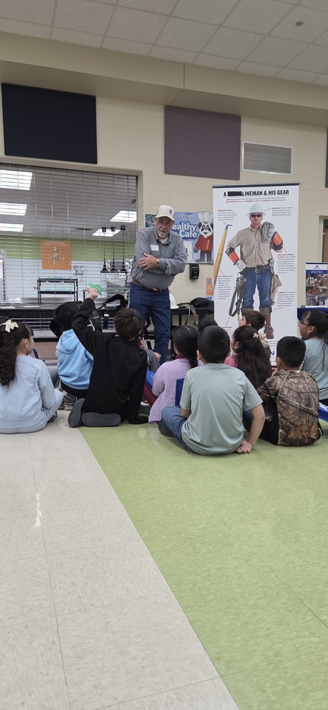 Speaker talks to seated elementary students about lineman career using poster display during classroom career day presentation.