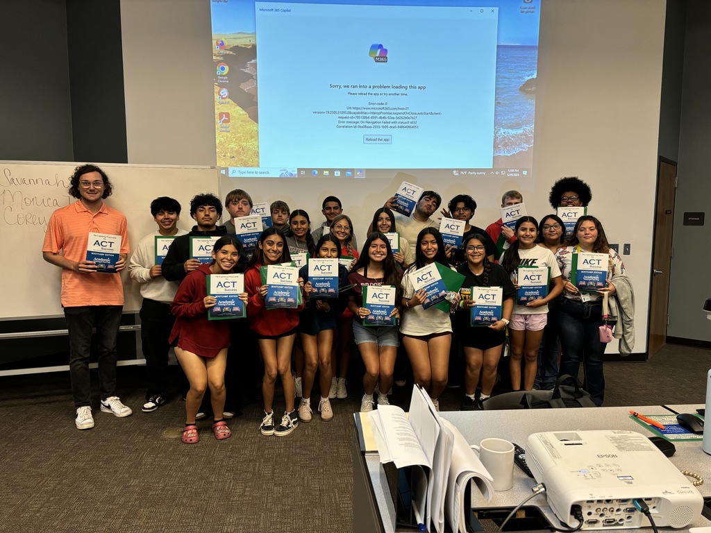 A group of smiling students hold certificates standing in front of a screen in a classroom.