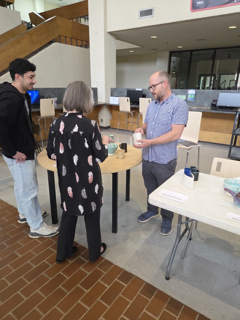 A man shows a piece of pottery to a woman and a smiling man.
