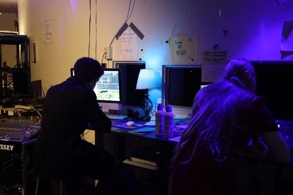 Two silhouettes of students running light and sound boards in the light booth.