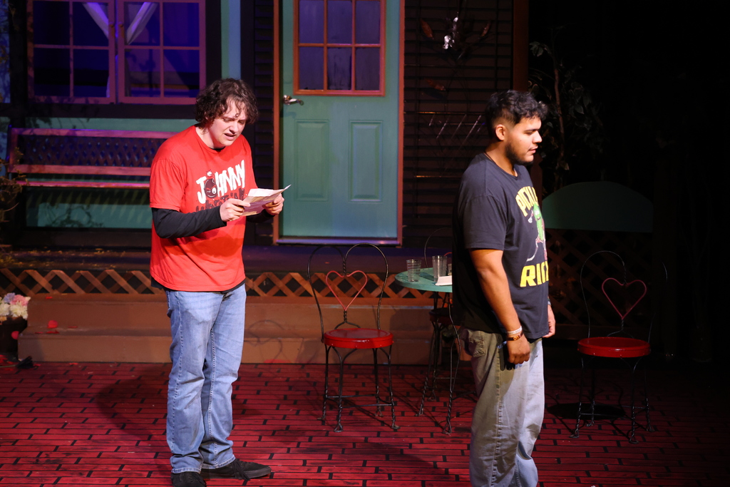 Two student actors perform dramatic scene on stage with patio set.